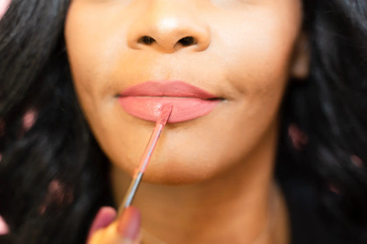 Person applying pink lipstick with a brush