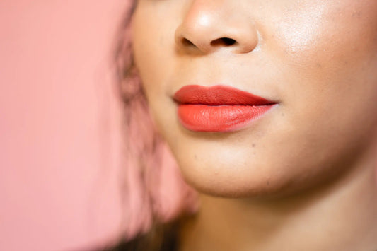 Close-up of a person wearing bright red orange lipstick on a blurred background
