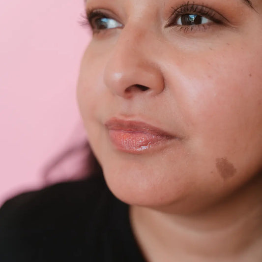 Close-up of a person's face with a pink background wearing a shimmery peach lip gloss