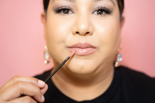 Woman applying lipstick with a brush against a pink background