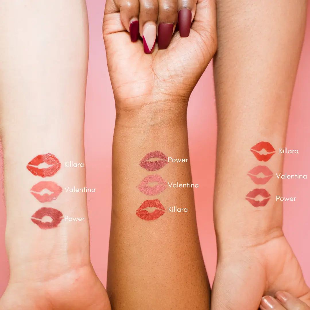 Three arms with lipstick swatches labeled 'Killara' and 'Valentina' on a pink background.