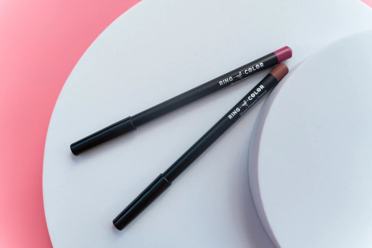 top view of lip liners branded with ring of color on circle prop with pink background