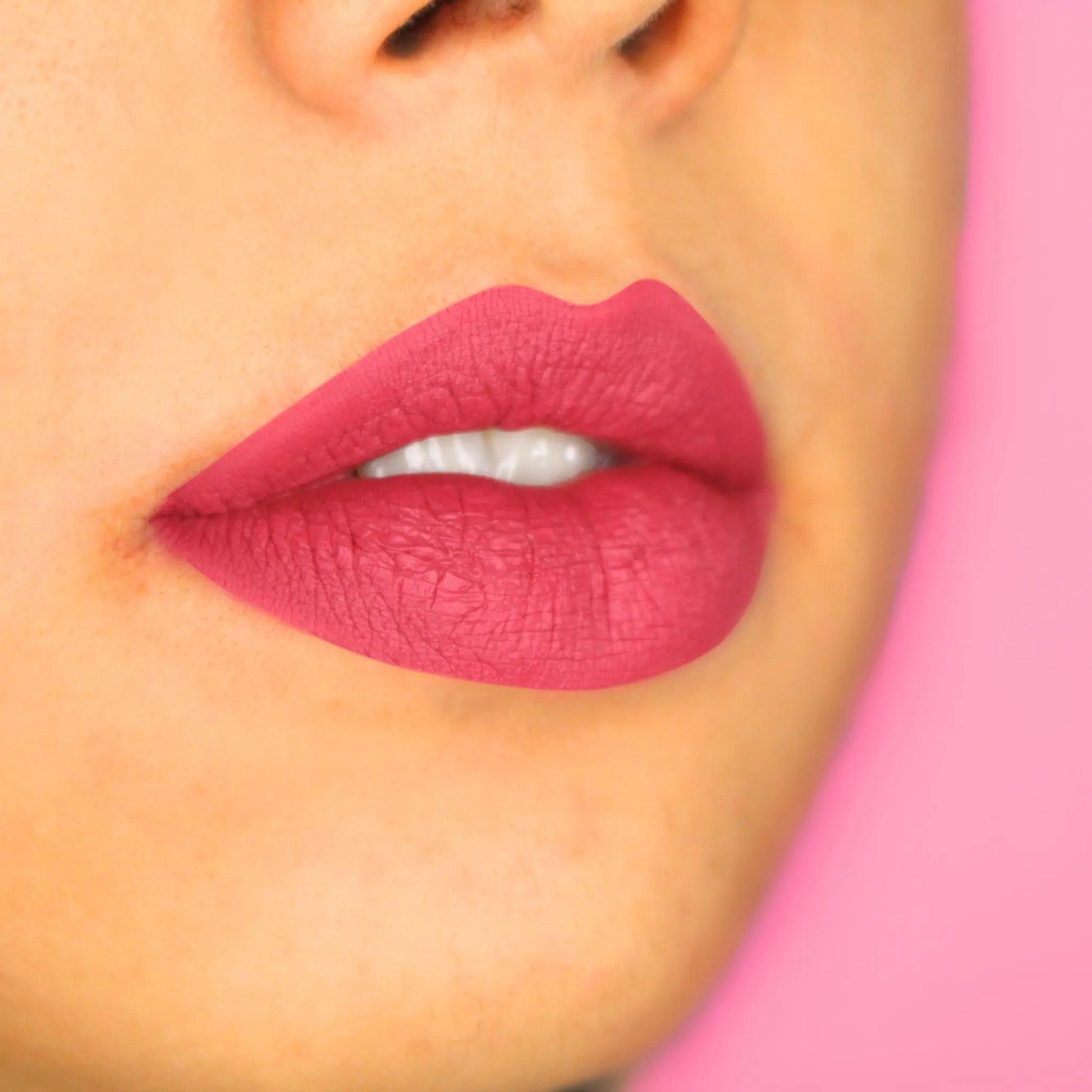 Close-up of a light skin person wearing bright pink lipstick with a pink background