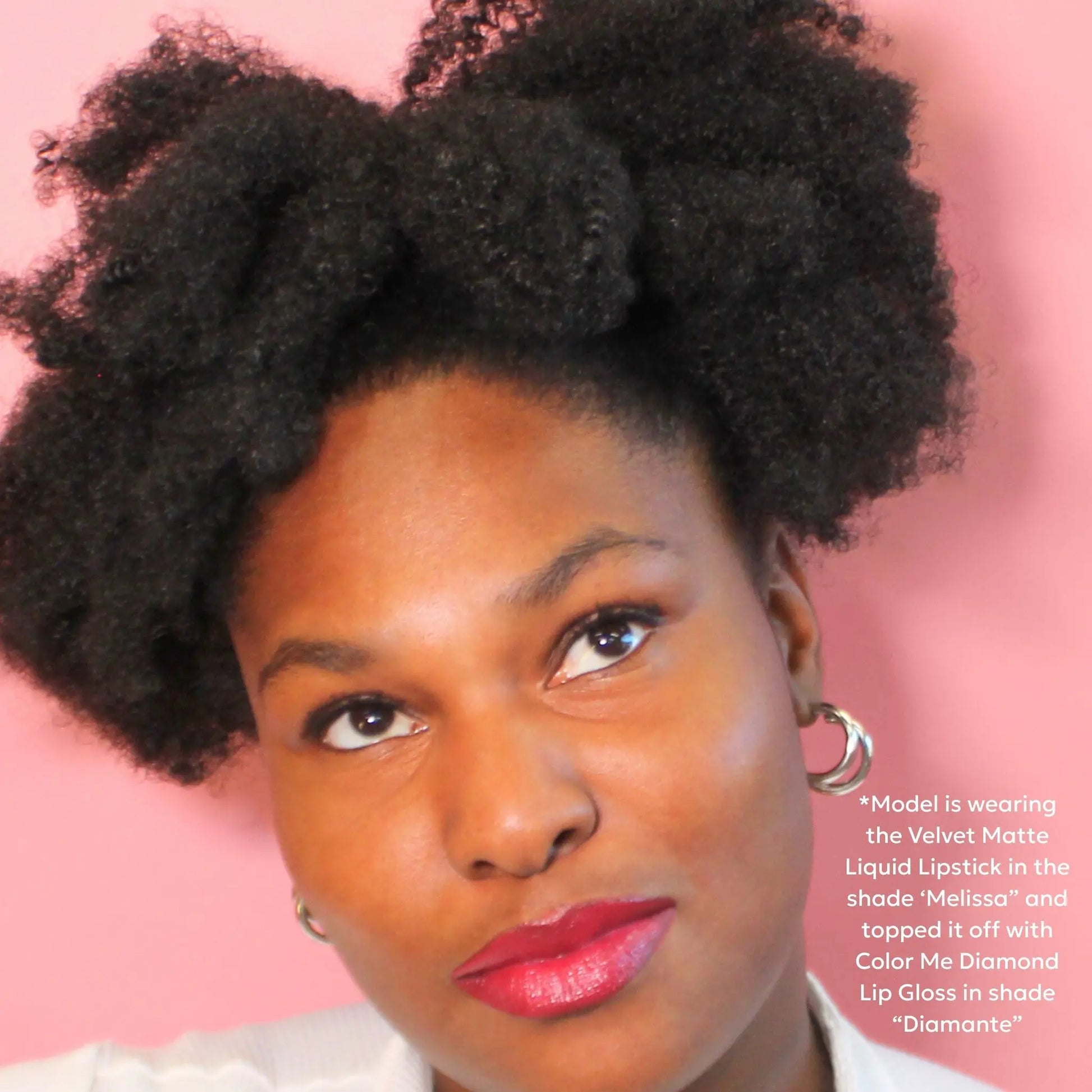 Woman with styled hair against a pink background, wearing makeup.