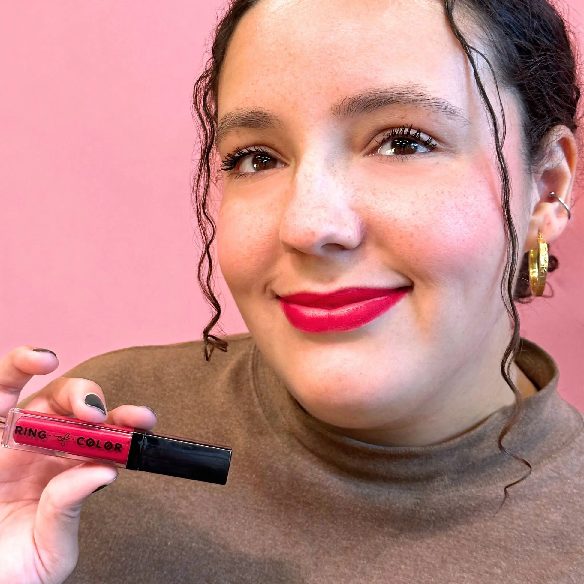 Woman with red lipstick holding a lip gloss against a pink background