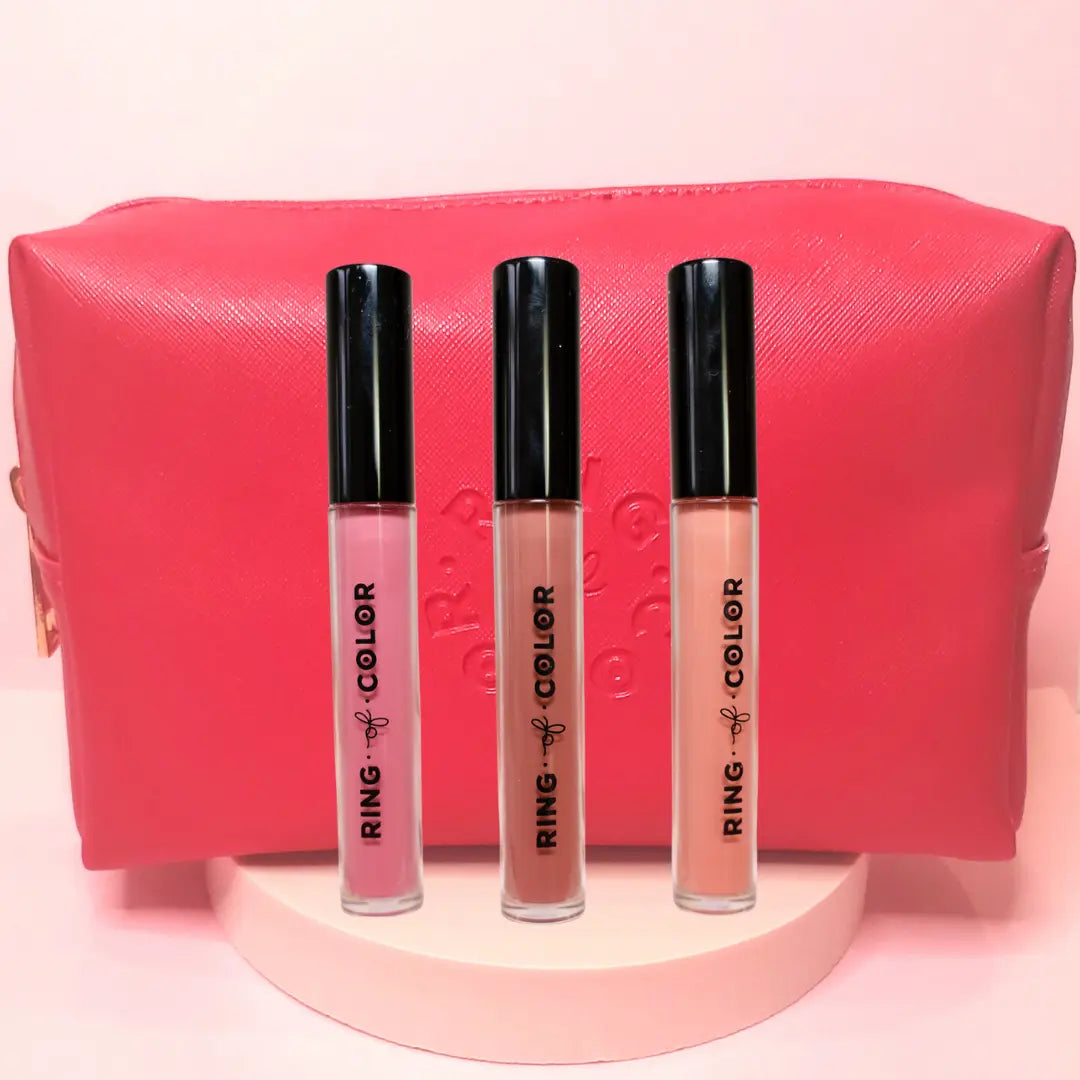 Three lip glosses with black caps in front of a pink pouch on a light pink background