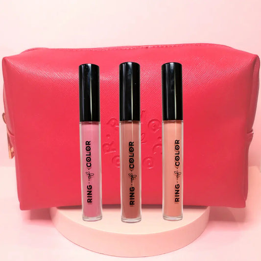 Three lip glosses with black caps in front of a pink pouch on a light pink background