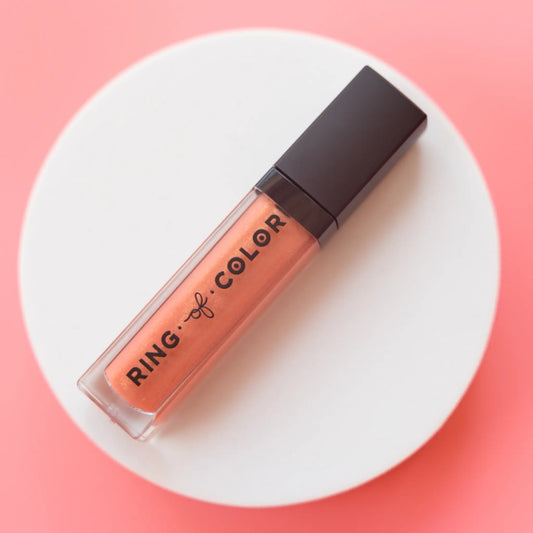 Peach shimmery Lip gloss with black cap on a white platform against a pink background