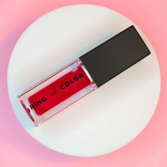 sheer Red lip gloss lip oil with black cap on a white platform against a pink background
