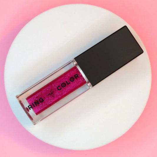 Pink glittery lip gloss with black cap on a white platform against a pink gradient background