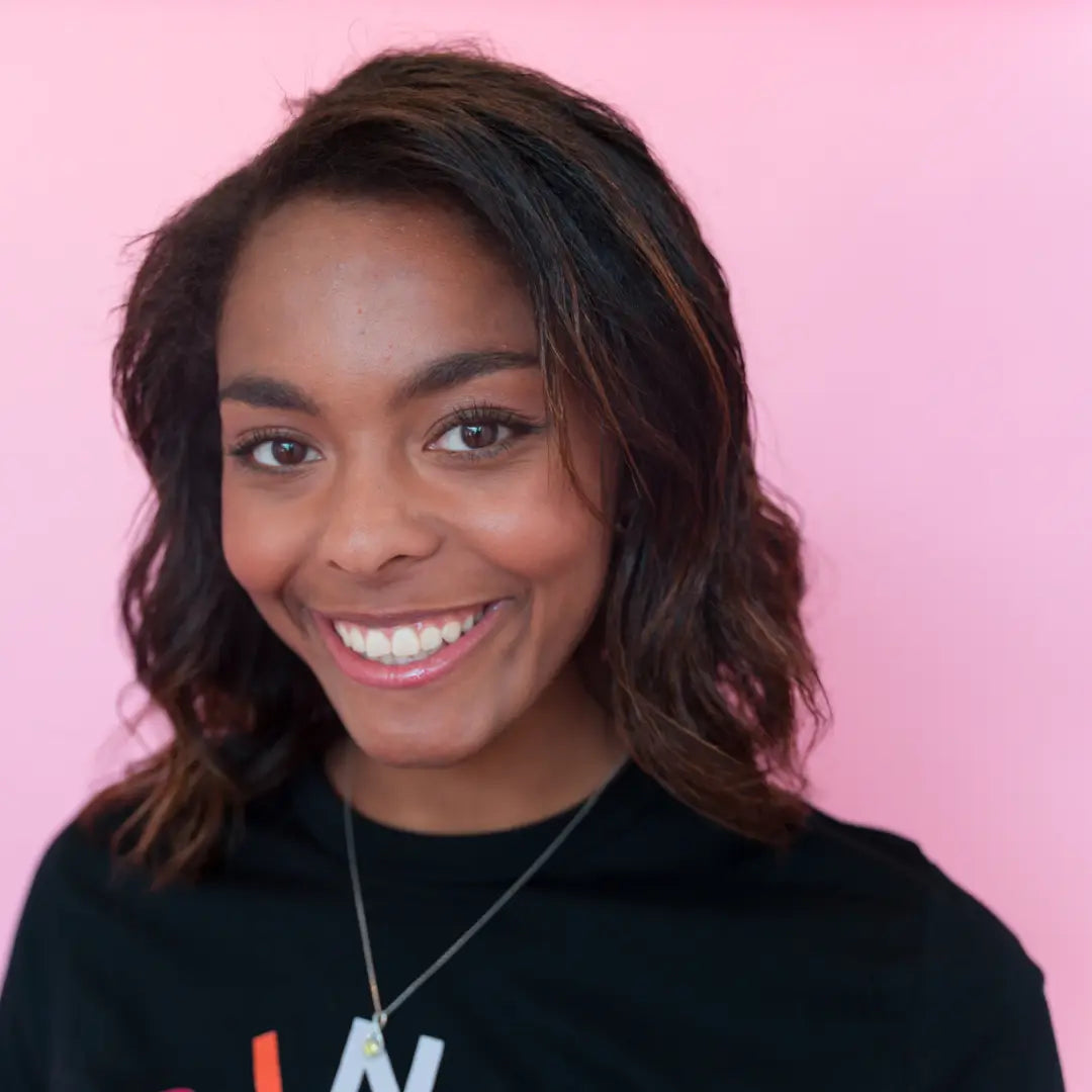 Woman wearing a black hoodie with visible text against a pink background
