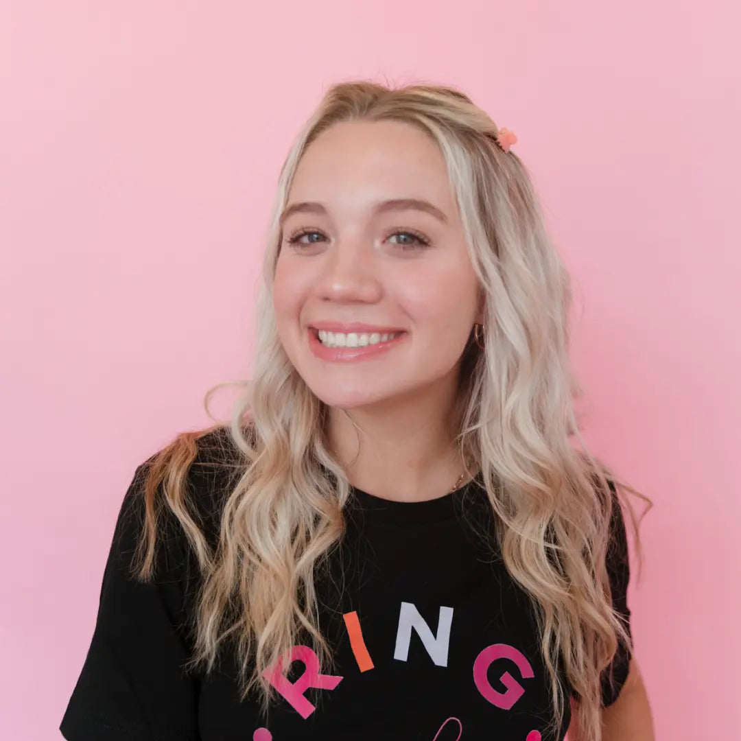 Person wearing a black shirt with colorful text against a pink background