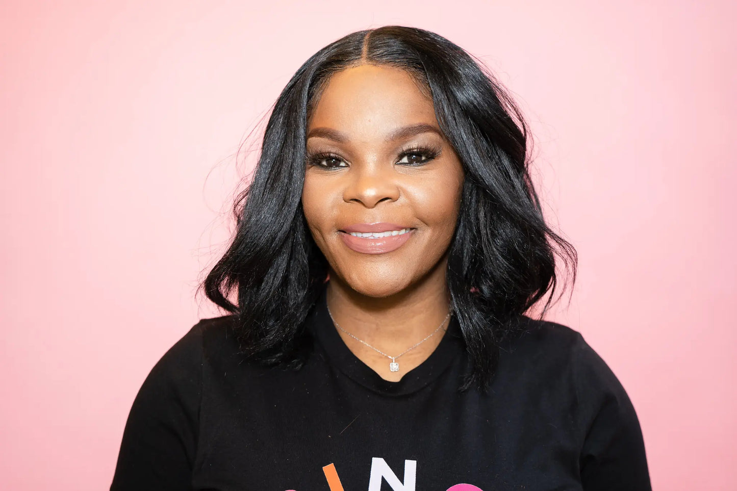 Woman wearing a black sweatshirt and a taupe medium brown lip lacquer with visible text on a pink background